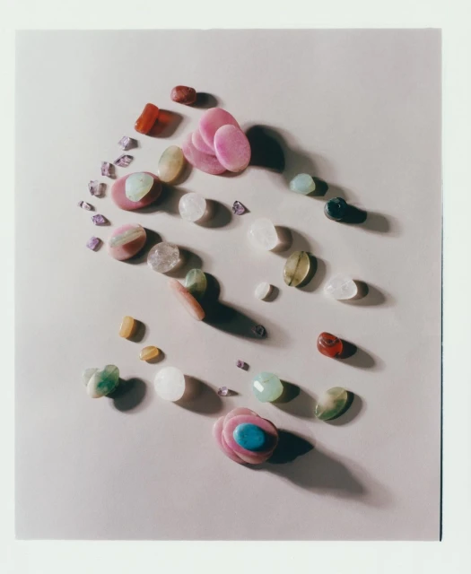 Overhead shot of assorted tumbled stones and polished gemstones in various colors, shapes, and sizes arranged on a neutral surface.