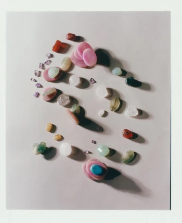 Overhead shot of assorted tumbled stones and polished gemstones in various colors, shapes, and sizes arranged on a neutral surface.