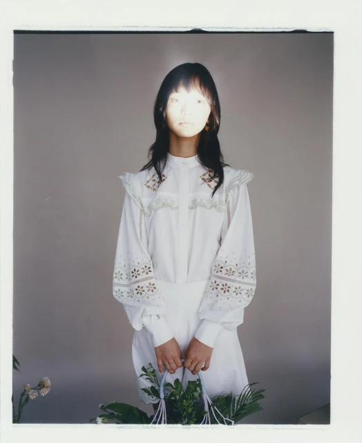 Asian woman in white vintage dress holding a floral arrangement against a grey backdrop with natural lighting and a photo studio environment.