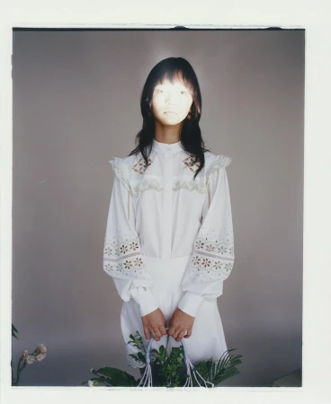 Asian woman in white vintage dress holding a floral arrangement against a grey backdrop with natural lighting and a photo studio environment.