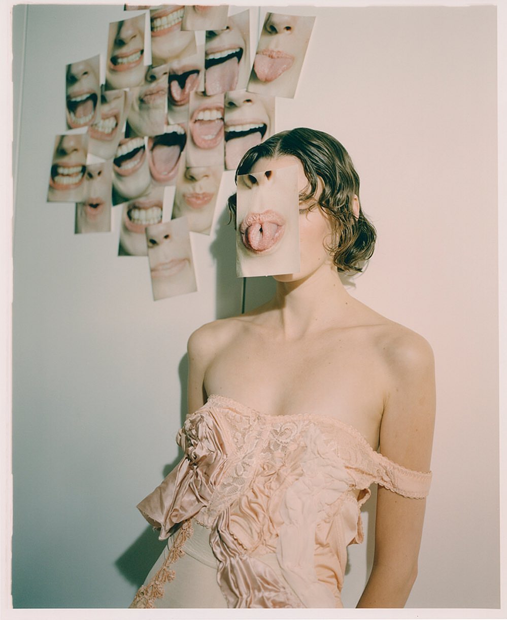 Woman in pink strapless dress posing in front of wall with photo prints of mouths expressing emotion, creative fashion photography.