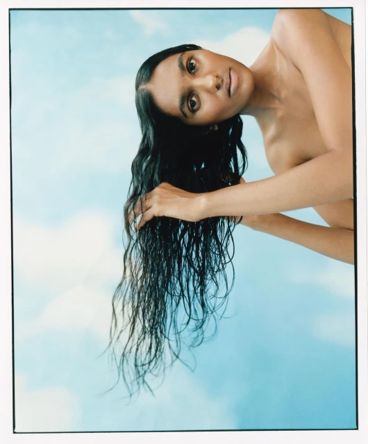 Adult woman with dark hair poses against a sky-blue cloud background, displaying beauty and style in a close-up studio shot.
