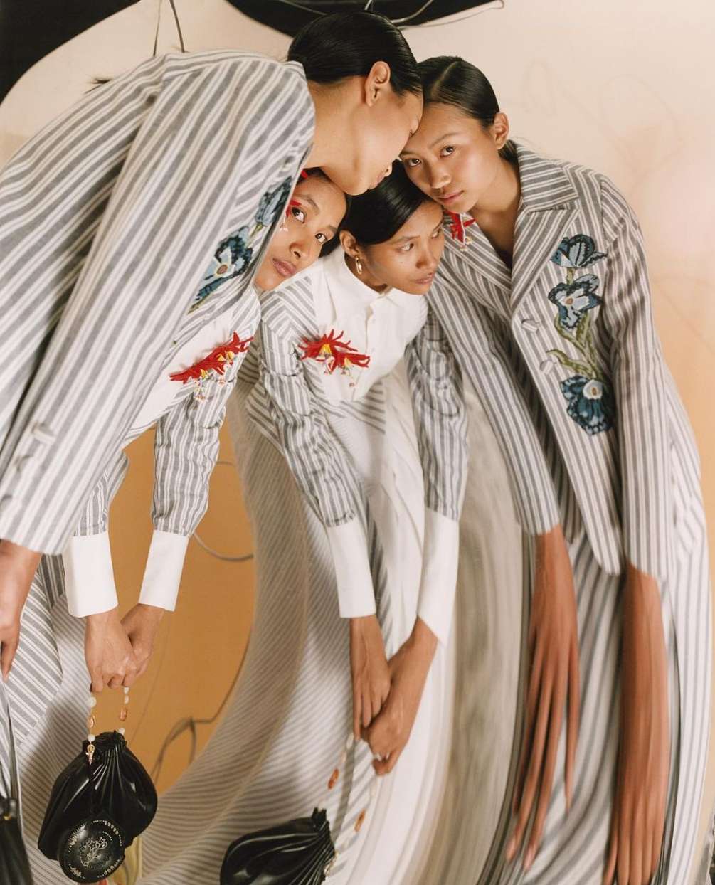 Fashion editorial shot of an Asian woman posing in a vertically striped jacket with floral embellishments in a photo studio with soft lighting.