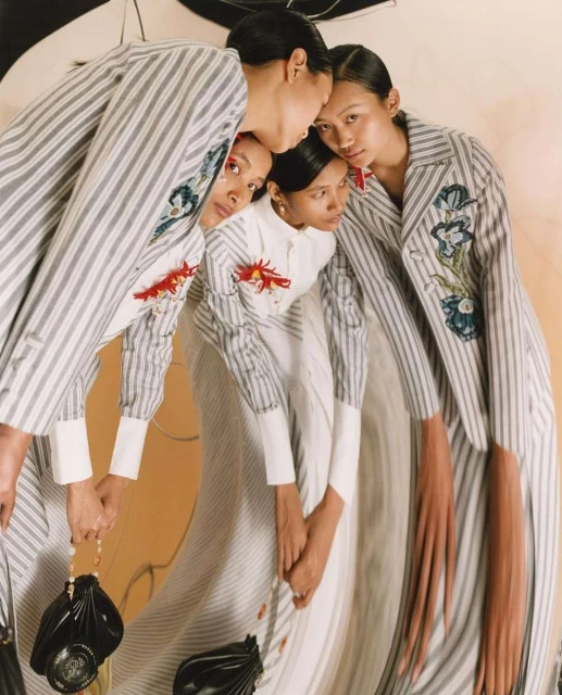 Fashion editorial shot of an Asian woman posing in a vertically striped jacket with floral embellishments in a photo studio with soft lighting.