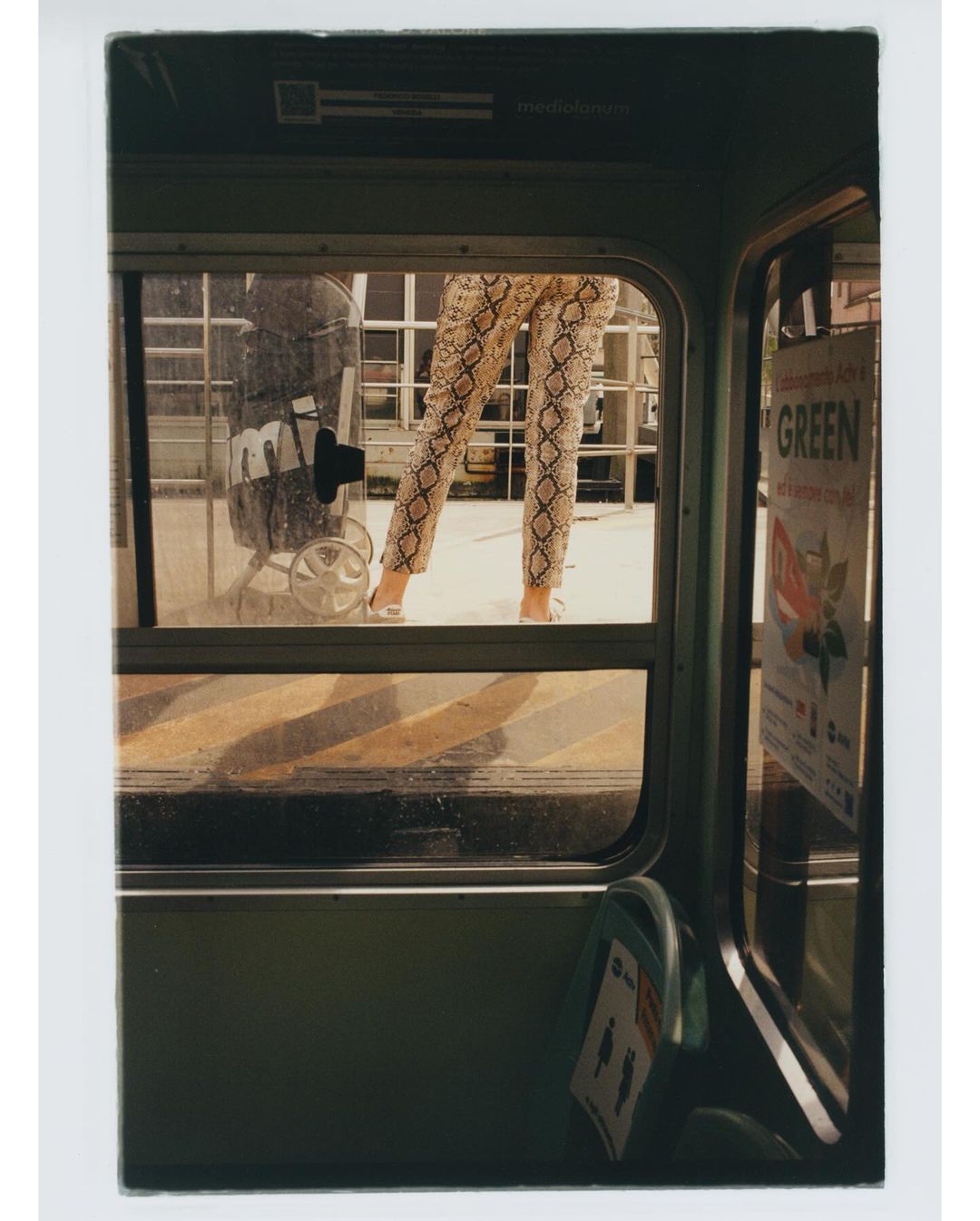Woman stands in the doorway of a bus wearing snake print pants. Trolley and GREEN sign visible in background, eye-level angle.