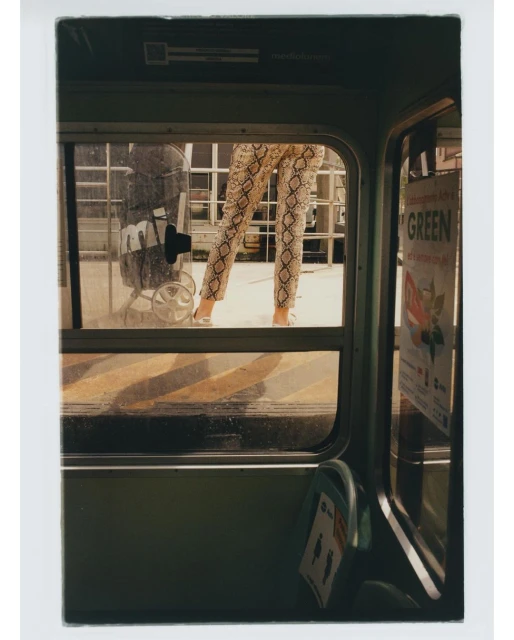 Woman stands in the doorway of a bus wearing snake print pants. Trolley and GREEN sign visible in background, eye-level angle.