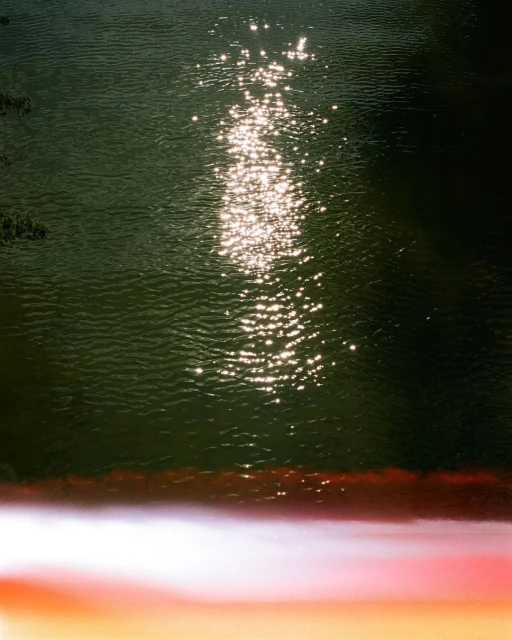 Overhead shot of a body of water reflecting sunlight, creating a sparkling effect on the dark green surface, with a blurred foreground.