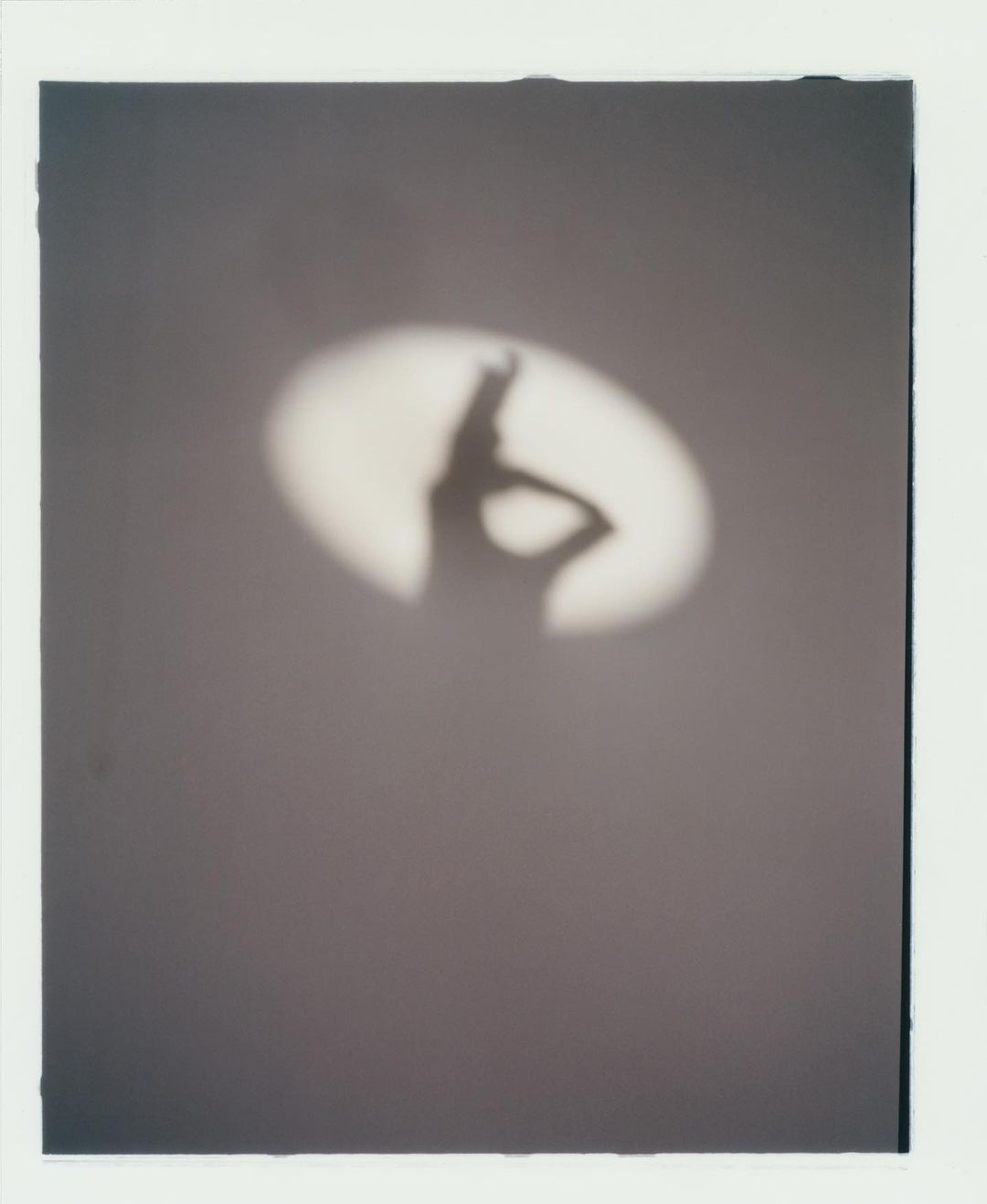 Silhouette of a person cast on a wall by a spotlight. The shadow figure strikes a pose with a hand on its hip.
