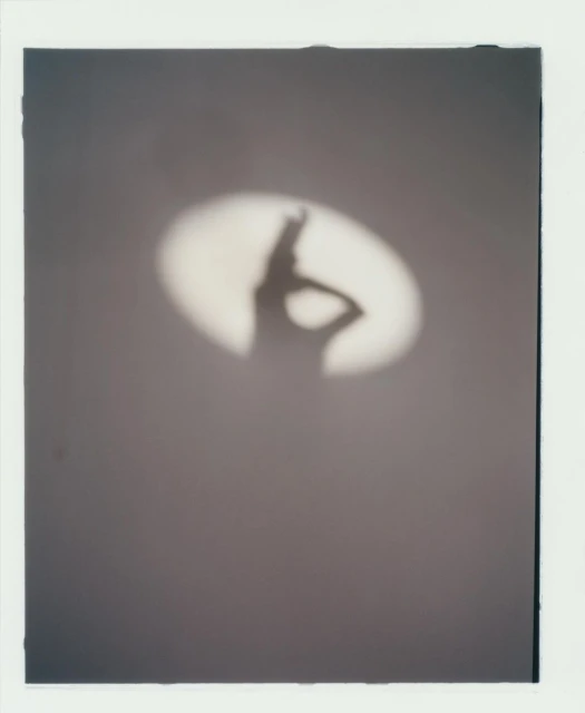 Silhouette of a person cast on a wall by a spotlight. The shadow figure strikes a pose with a hand on its hip.