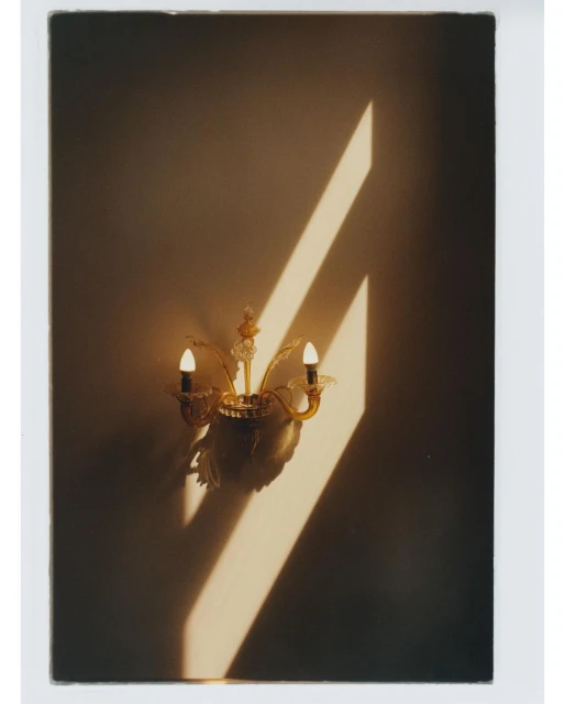 Illuminated sconce on a beige wall casts a geometric pattern of sunlight in an indoor space, creating warm ambiance.