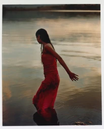 Woman in a red dress standing waist-deep in calm water at sunset by photographer Rid Burman