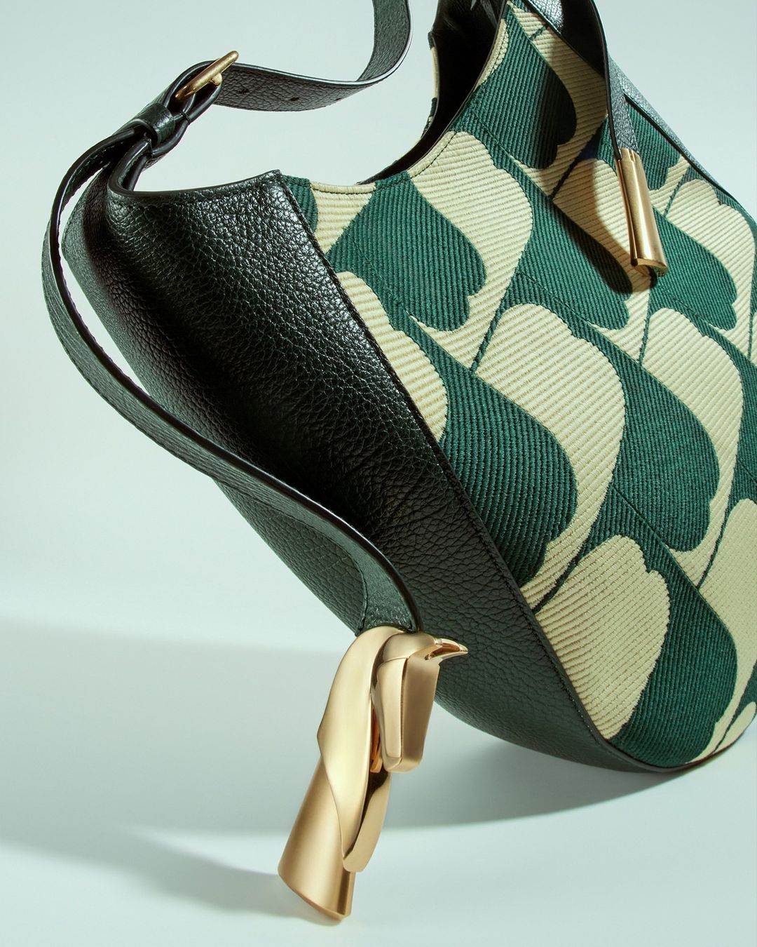 Close-up of a handbag with a distinctive green-and-cream ginkgo leaf pattern, black leather trim, and a stylized horse-head ornament.