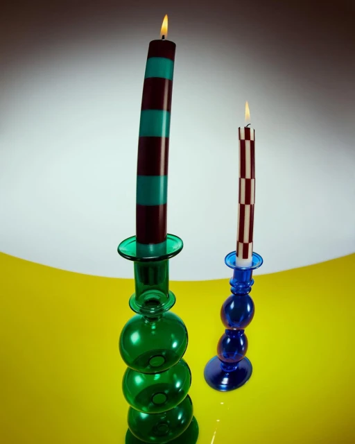 Two lit candles in decorative glass candle holders, one striped in brown and turquoise, the other checkered in brown and white.