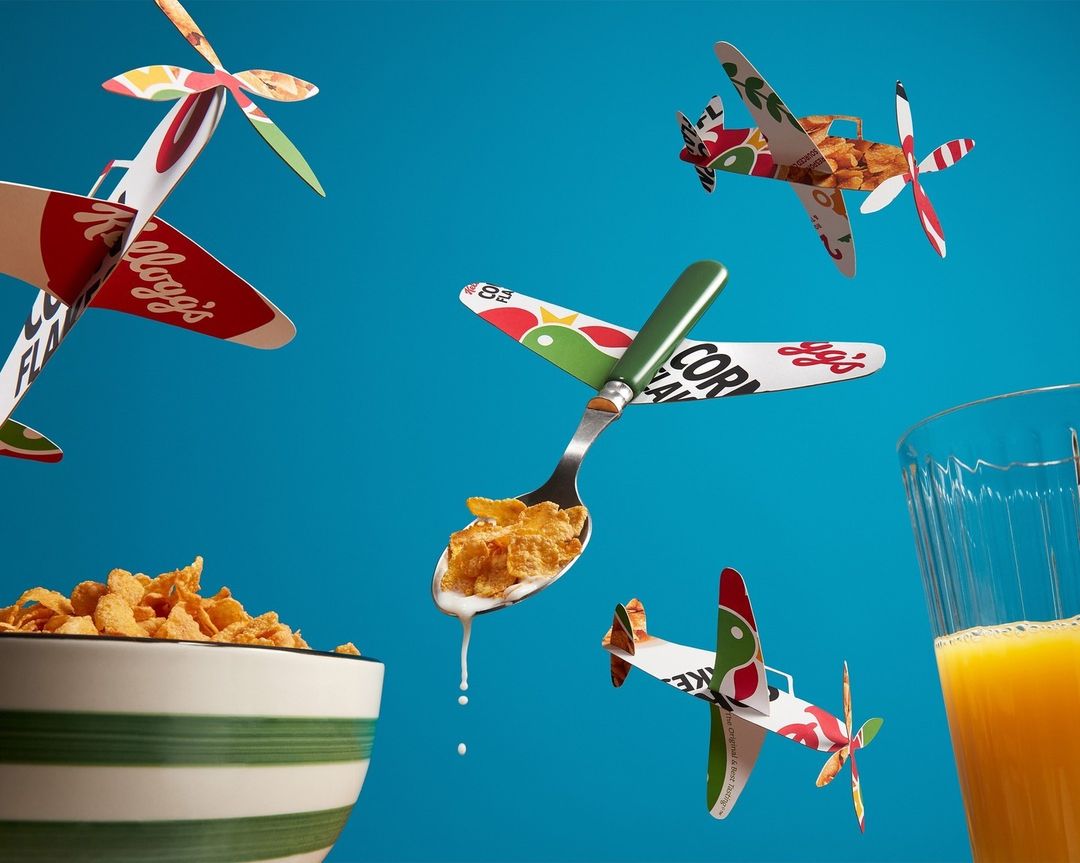 Still life of cereal in a bowl and orange juice with cereal box airplanes floating in a blue studio background for a food advertising concept.