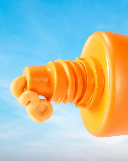 Bright orange sunscreen tube with a dollop of cream against a light blue sky, perfect for beauty, skincare, and summer vacation visuals.