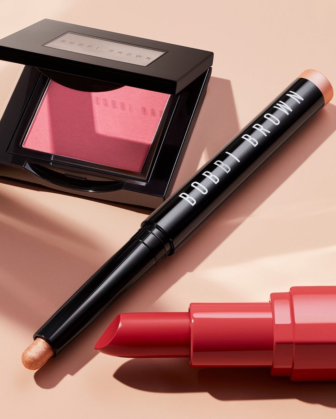 Bobbi Brown makeup including lipstick, blush, and eyeshadow stick on a neutral background for beauty and cosmetics marketing.