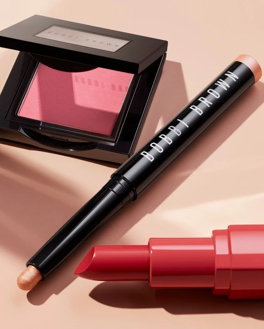 Bobbi Brown makeup including lipstick, blush, and eyeshadow stick on a neutral background for beauty and cosmetics marketing.