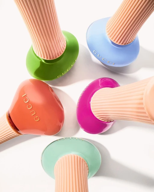 Overhead shot of pastel-colored Gucci nail polish bottles in shades of green, blue, pink, orange, and mint. Beauty and fashion concept.