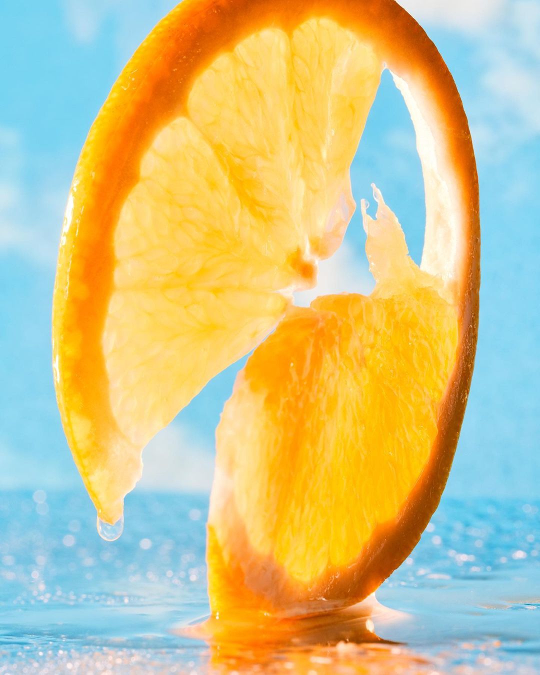 Close-up studio shot of two orange fruit slices with a water droplet against a blue background, highlighting the fruit's texture.