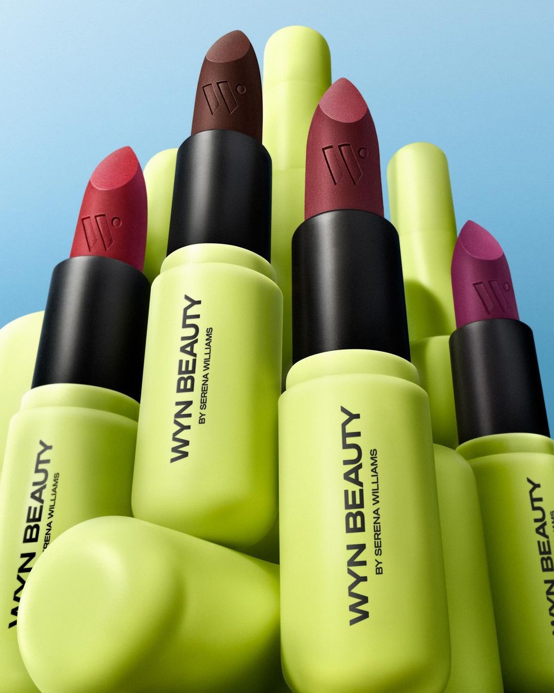 Wyn Beauty lipstick collection by Serena Williams displayed with bright neon green tubes and assorted colors on a blue background.