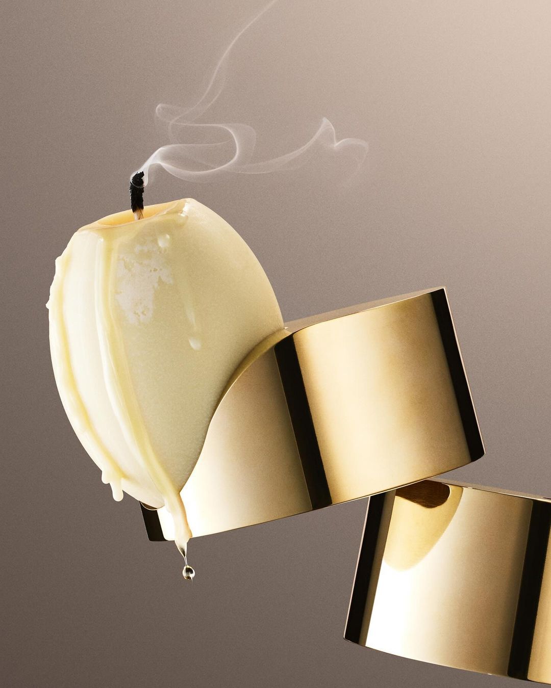 Elegant still life of an ivory candle with smoke on a gold stand against a gradient neutral background, showcasing minimalist home decor.