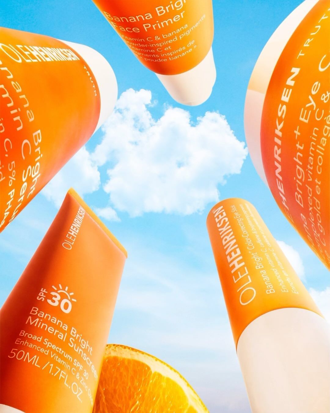 Ole Henriksen Banana Bright skincare products, including face primer, serum, sunscreen, and eye cream, are arranged against a blue sky.