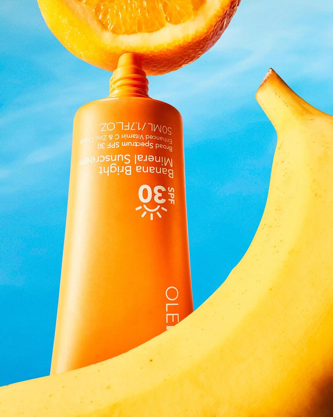 Ole Henriksen Banana Bright Mineral Sunscreen SPF 30 tube with orange and banana against a light blue background in a studio shot.