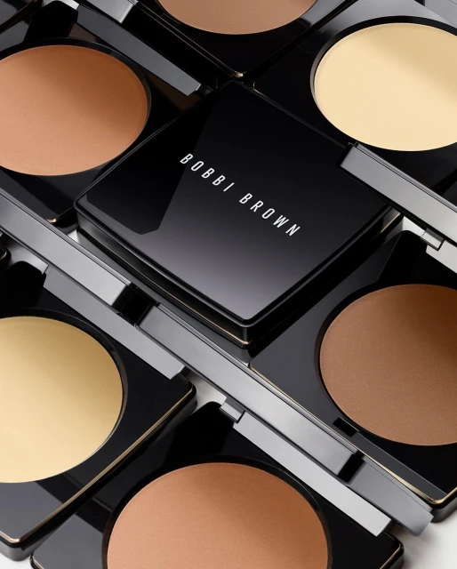 Arrangement of Bobbi Brown compacts in black packaging containing pressed powder in a range of skin tone shades.