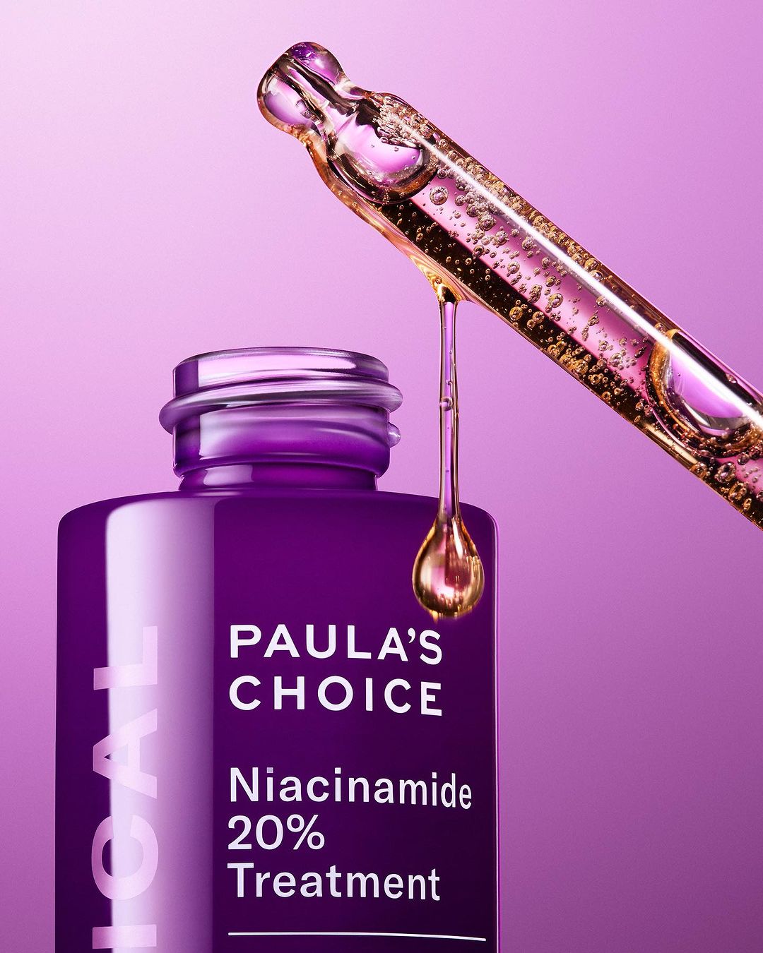 Close-up product shot of Paula's Choice Niacinamide 20% Treatment featuring serum dripping from a dropper over a purple container.