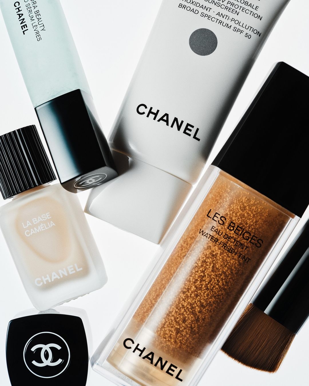 Several bottles and containers of Chanel makeup products are grouped together on a white surface. Product includes serum, foundation, sunscreen.