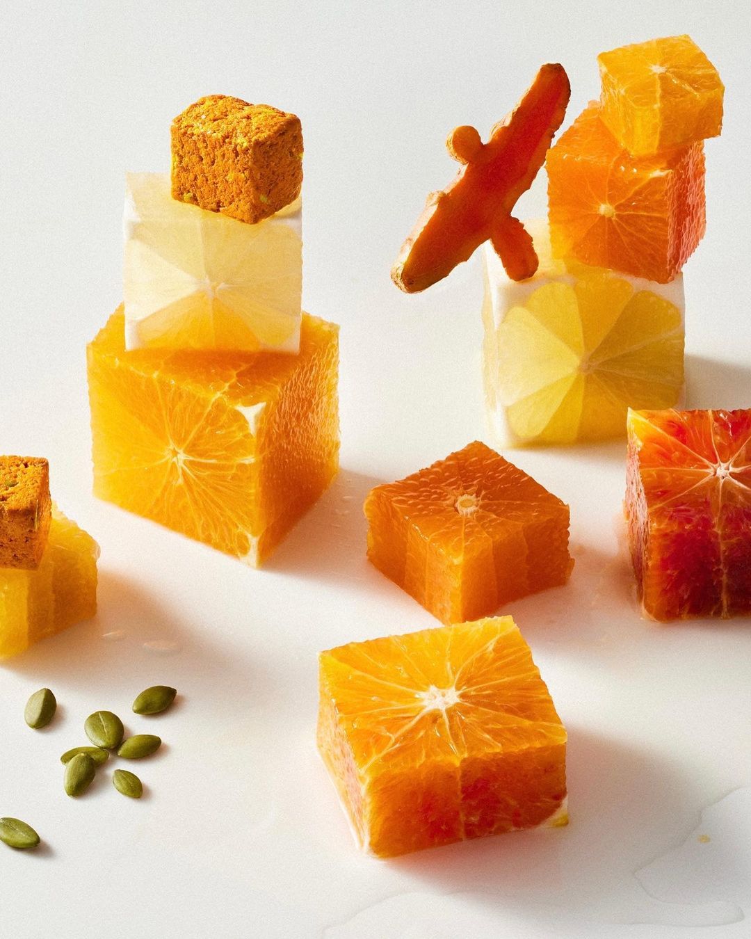 Cube-shaped orange slices and turmeric root pieces are stacked against a white background in a studio food photography composition.