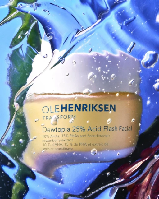 Ole Henriksen Dewtopia facial product jar against a backdrop of blue and green hues, enhanced with water droplets for a fresh aesthetic.