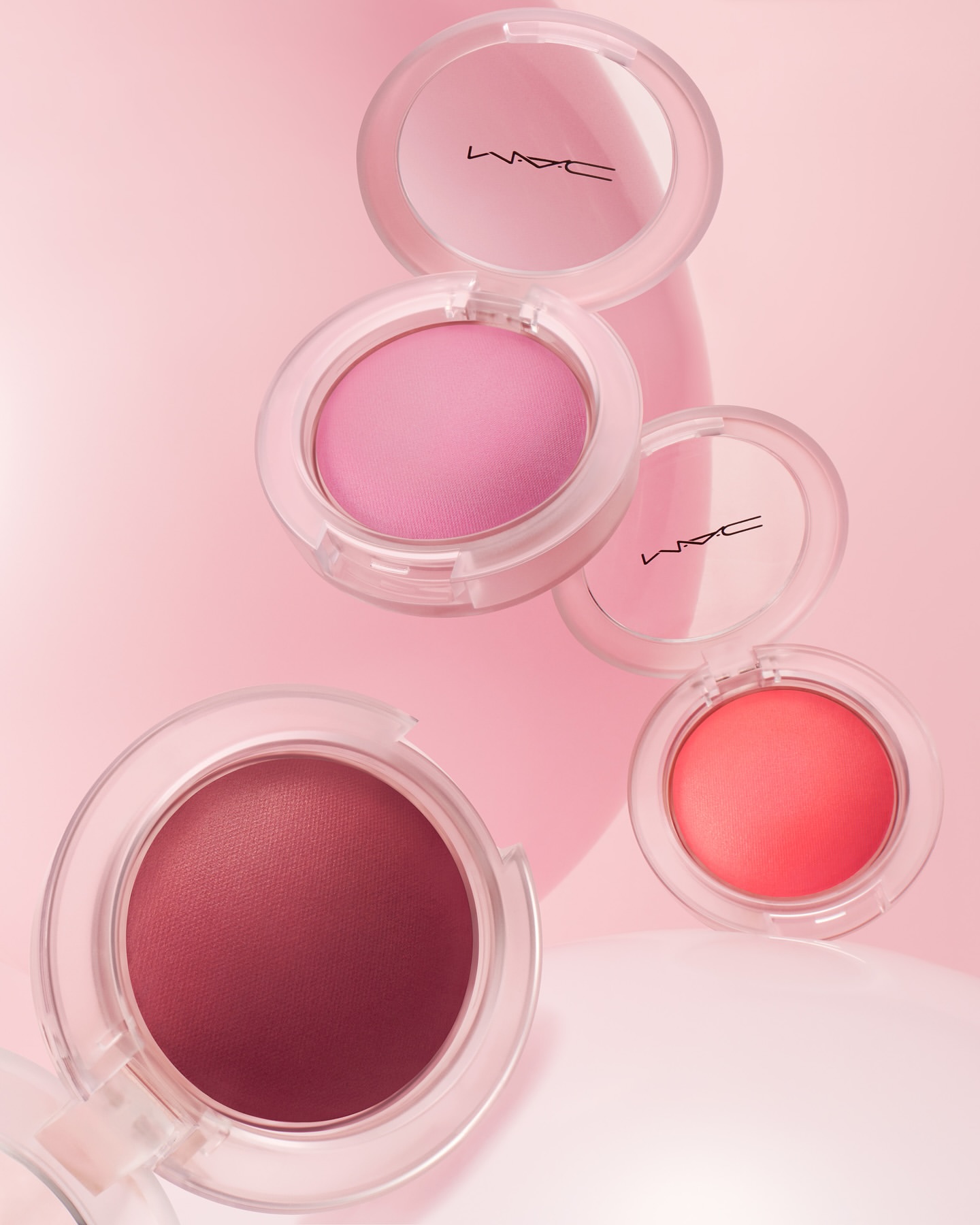 Beauty still life of MAC cosmetics blush compacts in shades of pink, peach, and rose with a soft pink background and diffused lighting.