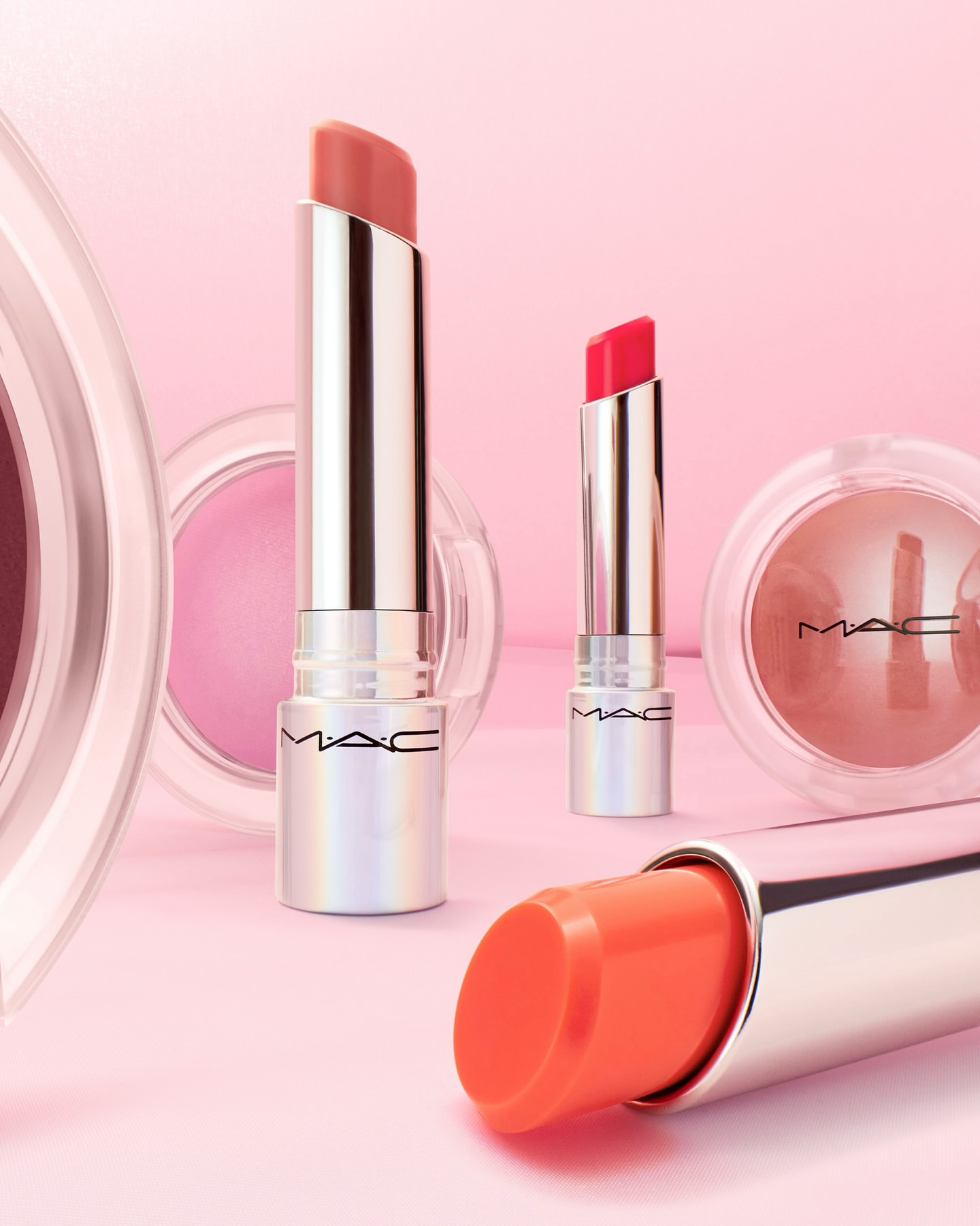 MAC lipsticks and powder blush displayed on a pink surface, showcasing a range of colors and textures against a soft pink background.