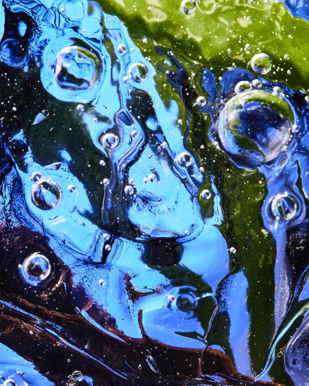 Macro shot of abstract translucent blue and green liquid or gel with bubbles, creating an otherworldly and textured effect.