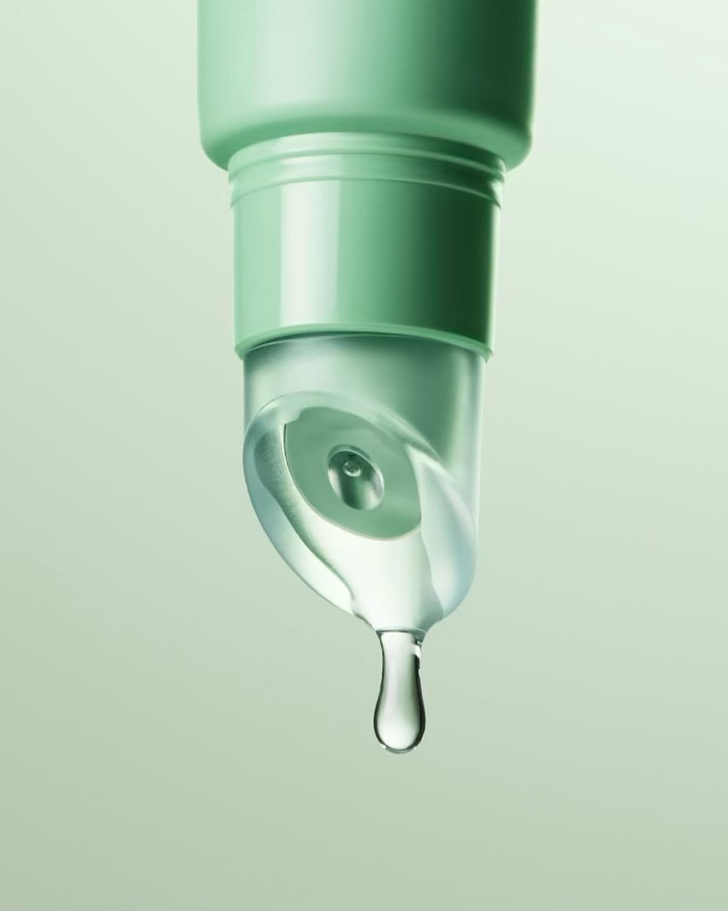 Close-up of a green tube dispenser with a clear liquid and a single water droplet falling in a light green studio backdrop.