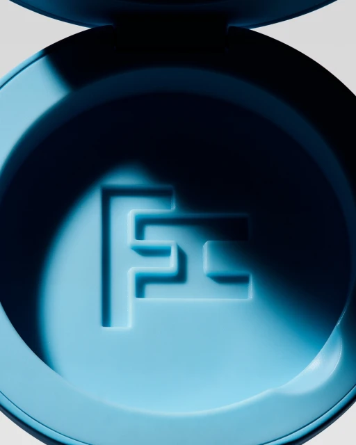 Close-up of a light blue round container with embossed initial 'F' logo against a bright neutral background, emphasizing minimalist design.
