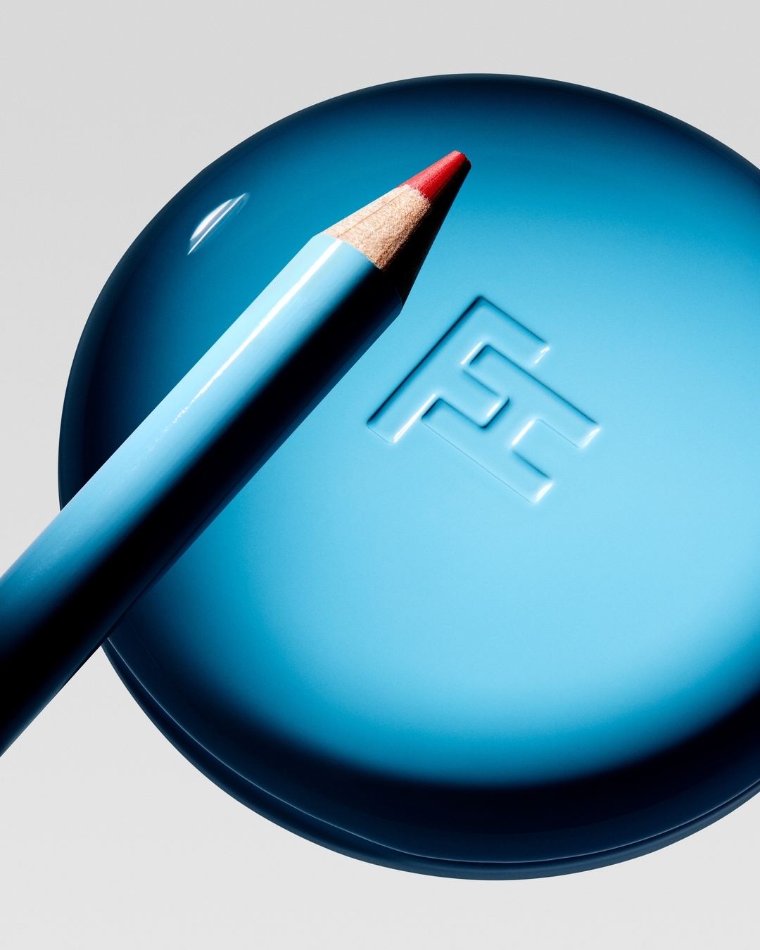 Close-up of a light blue eyeliner pencil with a red tip placed diagonally on top of a blue compact case with an embossed logo.