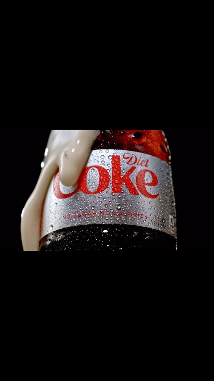 Close-up of a Diet Coke bottle with condensation and foam. The iconic logo and silver can are prominently featured against a black background.
