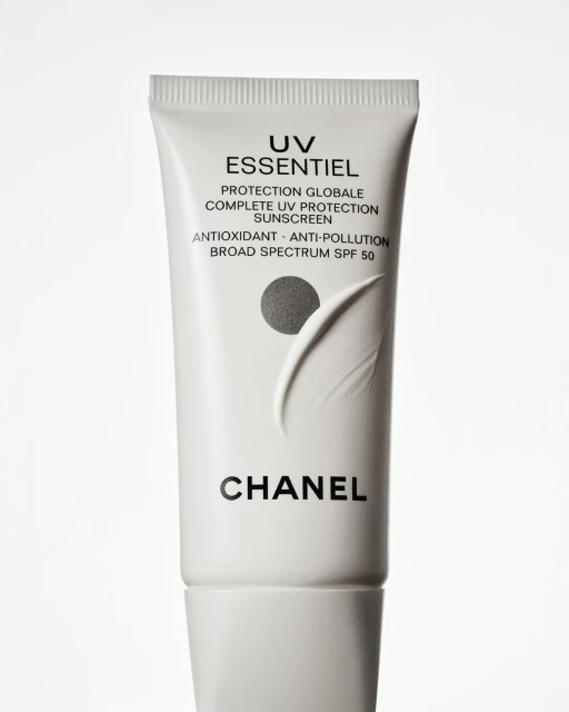 Chanel UV Essentiel sunscreen tube on a white background. A white tube with black lettering is centered in a vertical format.
