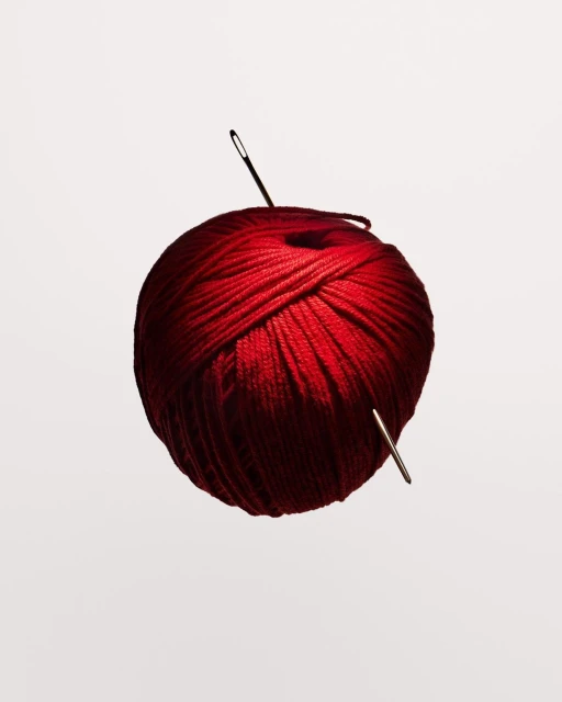 Red yarn ball with sewing needles on a white background in a studio shot, showcasing texture and crafting materials.