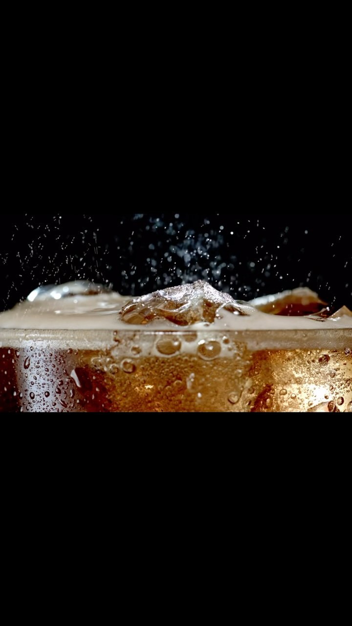 Refreshing dark soda with ice cubes in a glass. Bubbles and condensation add to the cool beverage in a black background.
