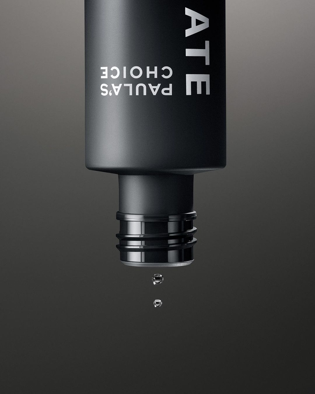 Close-up of a black Paula's Choice bottle with water droplets falling, set against a dark gray background, showcasing skincare.