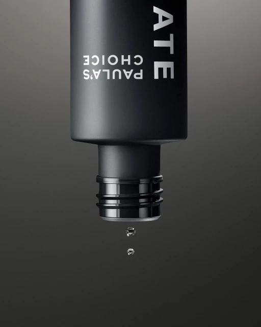 Close-up of a black Paula's Choice bottle with water droplets falling, set against a dark gray background, showcasing skincare.