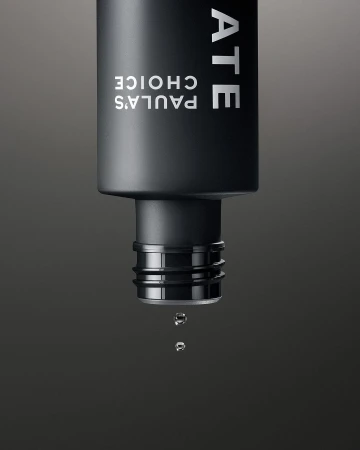 Close-up of a black Paula's Choice bottle with water droplets falling, set against a dark gray background, showcasing skincare.