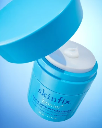Open light blue container of Skinfix Triple Lipid-Peptide Cream with a blob of white cream, all against a graduated blue background.