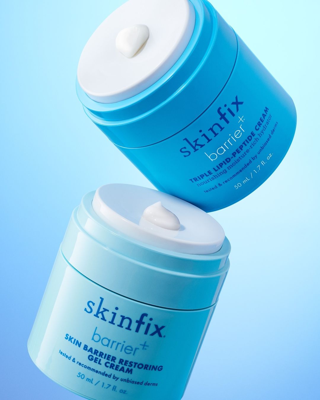 Two jars of Skinfix Barrier+ cream stacked, showcasing skincare product with a white cream dollop on the lid against a blue gradient background.
