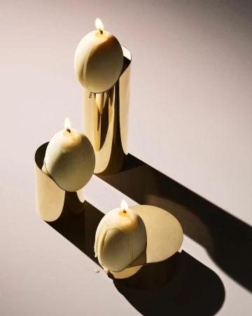 Three lit candles in gold holders on a light surface casting a shadow, ideal for product photography or home decor concepts.