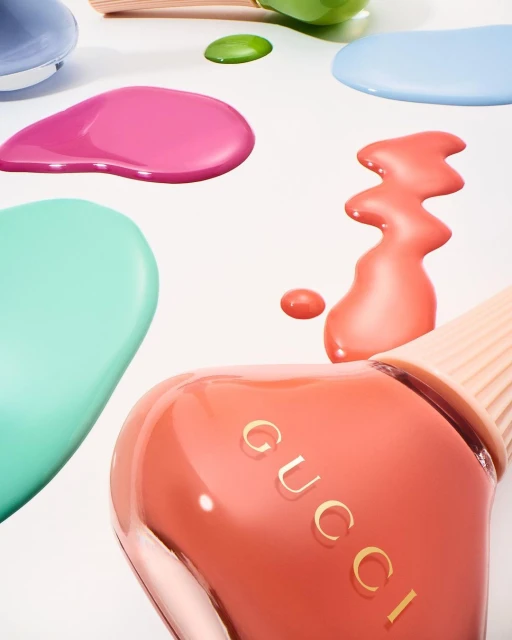 Close-up of Gucci nail polish bottles in peach and mint with colorful scattered drops on a white surface, beauty product shot.
