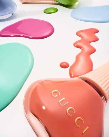 Close-up of Gucci nail polish bottles in peach and mint with colorful scattered drops on a white surface, beauty product shot.